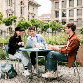 3 Studierende sitzen diskutierend draussen an einem Tisch